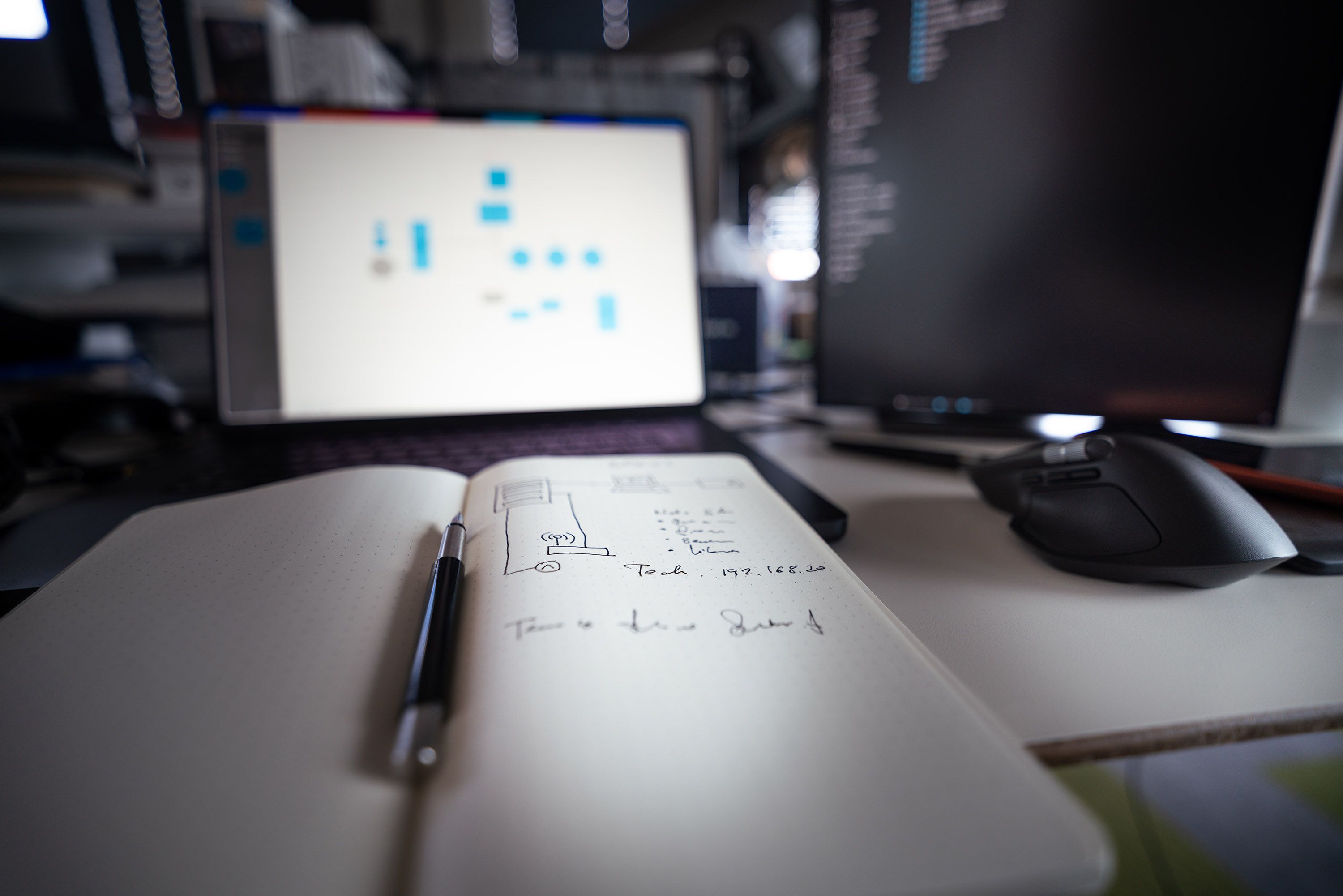 A minimalist studio workspace with an open notebook, a pen, and a green plant on a wooden desk.